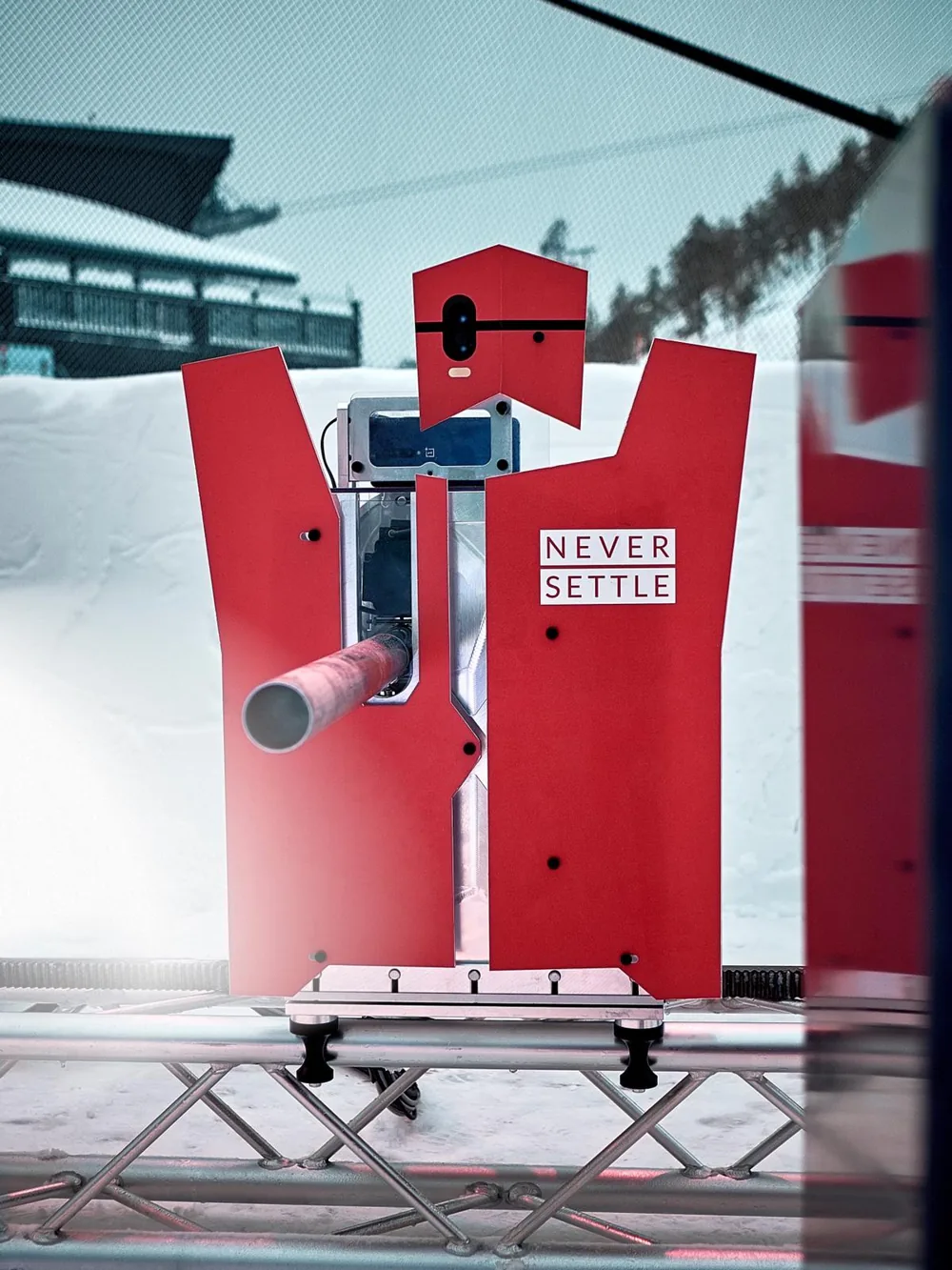 Red OnePlus Never Settle snowball-throwing robot on a snowy set