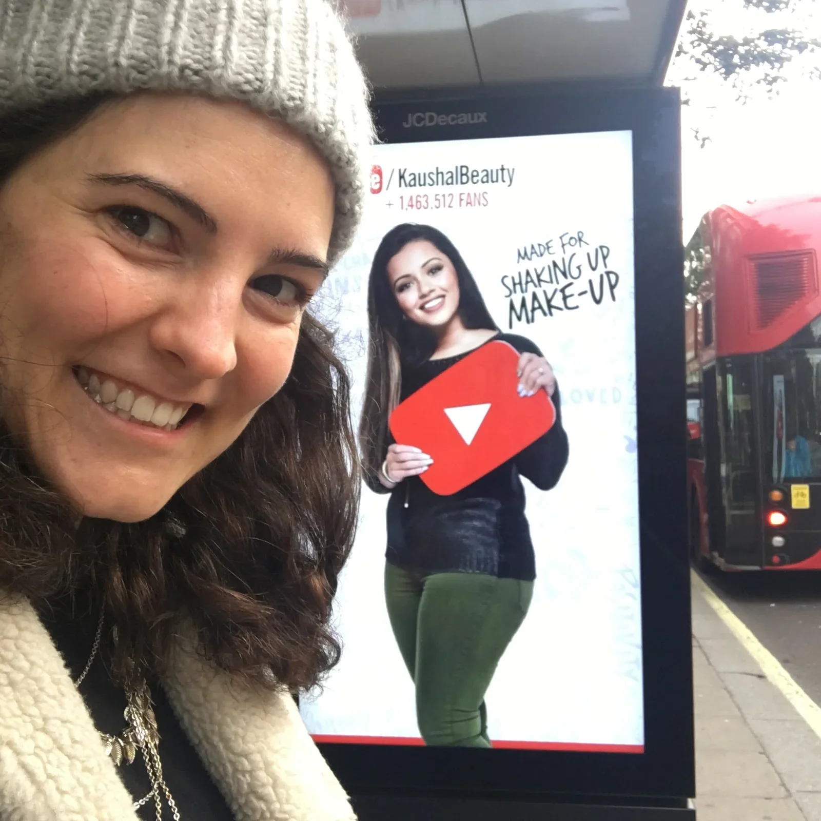 Kate taking a selfie next to a Made For You bus shelter ad for KaushalBeauty